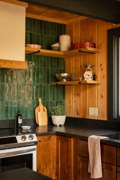 a kitchen with green tiles and wooden shelves on the wall, along with black counter tops