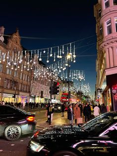 people are walking down the street in front of buildings with lights strung from it's sides