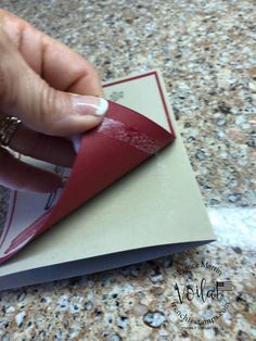 a hand holding a red piece of paper on top of a white and gray envelope