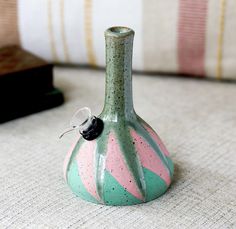 a green vase sitting on top of a table next to a pillow with a small black object in it