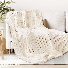 a white blanket sitting on top of a couch next to a potted plant