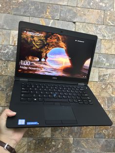 a person holding up a laptop computer in front of a stone wall