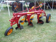 a red and yellow tractor sitting on top of a grass field next to a tent