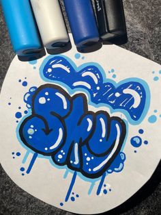 three blue and one white spray paint bottles on top of a skateboard with graffiti written on it