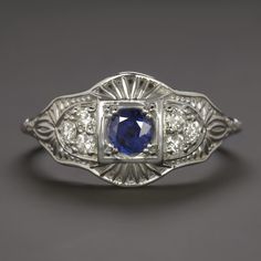 This beautiful and unique ring features a richl blue sapphire set in a diamond studded vintage style design that will never go out of style! The sapphire has a richly saturated blue hue that contrasts strikingly with the 14k white gold setting. Utterly classic and romantic, the antique style setting is richly textured Art Deco Platinum Sapphire Ring, Art Deco Platinum Sapphire Ring With 17 Jewels, Classic Blue Diamond Ring, Classic Blue Diamond Ring With Accents, Blue Platinum Jewelry With Single Cut Diamonds, Platinum Jewelry With Blue Single Cut Diamonds, Blue Single Cut Diamond Jewelry In Platinum, Vintage Platinum Diamond Ring With Gemstone, Art Deco Blue Diamond Ring With Center Stone