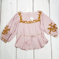 Gorgeous Bohemian Festival Top From Free People. Features A Flattering Square Neckline, Gorgeous 3/4 Lenght Puff Sleeves Finished With An Embroidered Button Cuff, Tie Waist With Tassel Rope And Lush Gold Embroidery Detailing. A Chic And Comfortable Cotton/Rayon Blend. Hand Wash. Color Is Pink/Rose, A Light Lavender-Pink Color With Lush Gold Embroidery. New With Tags. Size Medium. Measurements Taken Flat And Are Approximate: Bust 18", Adjustable Waist Up To 20", Length 23", Sleeve 19". Pink Embroidered Feminine Blouse, Pink Feminine Embroidered Blouse, Pink Feminine Embroidered Top For Spring, Spring Pink Embroidered Feminine Top, Spring Pink Embroidered Blouse, Spring Embroidered Pink Blouse, Pink Bohemian Cotton Top, Pink Bohemian Tops For Spring, Fitted Pink Bohemian Blouse