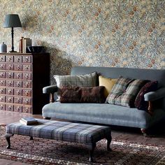 a couch and ottoman in a room with wall paper on the walls, rugs and drawers