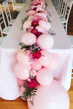 a long table with white chairs and pink balloons on the top, along with flowers and greenery