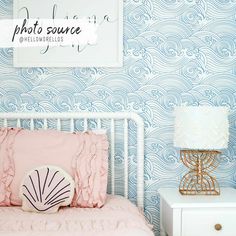 a white bed sitting next to a wall with blue waves on it and a pink pillow