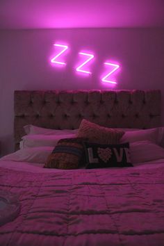 a bed that has some pillows on it in front of a neon sign above it