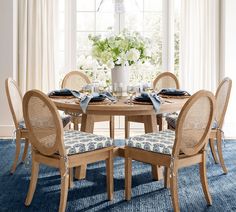 a dining room table set with chairs and place settings in front of a large window