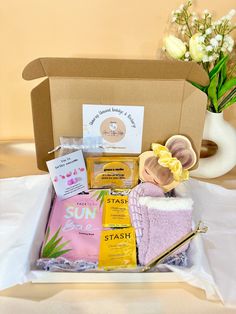 an open box with various items in it sitting on a white table cloth next to a vase and flowers