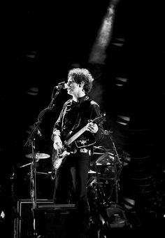 a man standing on top of a stage with a guitar in front of him and microphone to his side