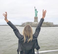 a woman with her hands up in front of the statue of liberty