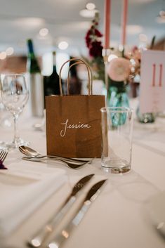 the table is set with silverware, wine glasses and a brown paper bag on it