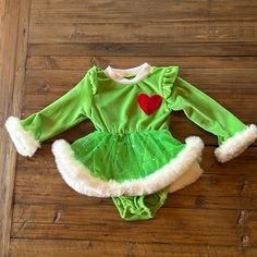 a green and white outfit with red heart on the chest sitting on a wooden floor