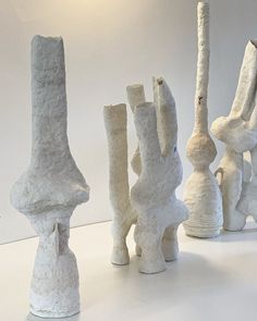 several white vases are lined up in a row on the table, one is made out of clay