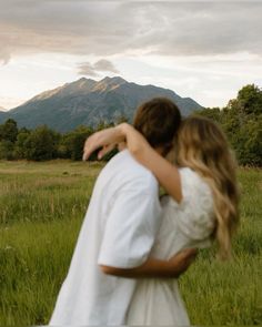 a man and woman hug in the middle of a field with mountains in the background