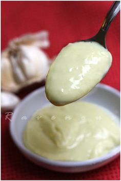 a spoon full of mayonnaise and garlic on a red tablecloth with cloves in the background