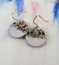 a pair of earrings with colorful dots on them sitting on top of a white surface