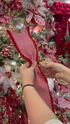 someone is decorating a christmas tree with red and white ribbons