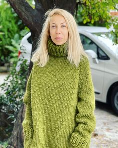 a woman standing in front of a tree wearing a green turtle neck sweater and jeans