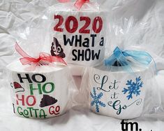 three ceramic mugs decorated with christmas sayings and bows are sitting on a white sheet