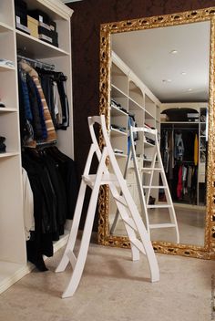 a large mirror sitting on top of a white shelf next to a closet filled with clothes