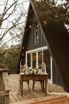 a table with candles and flowers on it in front of a house that has lights strung from the roof