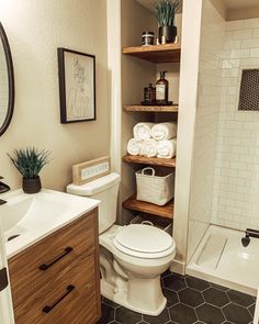 a white toilet sitting in a bathroom next to a sink and bathtub with shelves above it