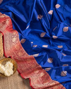 "Color : Royal Blue with Red. Pure Banarasi Katan silk saree in ink-blue, adorned with white brocades and flanked by golden floral Tilfi work on red borders and pallu, paired with a red brocade blouse sequin-embroidered on the sleeves and neck. Kanchipuram silk saree in maroon with white brocades and golden borders, paired with a self-colored brocade blouse. This saree is for sure to look even more stunning when worn for any occasion.  This saree is very easy to drape and falls elegantly making Blue And Red Saree, Royal Blue Banarasi Saree, Blue Blouse Piece For Eid Puja, Royal Blue Saree For Diwali, Unstitched Royal Blue Saree, Blue Raw Silk Dupatta For Puja, Blue Raw Silk Blouse Piece For Festivals, Unstitched Blue Blouse Piece For Traditional Ceremonies, Blue Blouse Piece With Traditional Patterns For Festivals