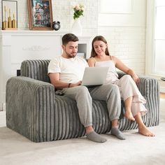 a man and woman sitting on a couch looking at a laptop