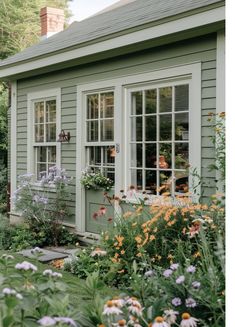 a green house with lots of flowers in the front yard and windows on each side