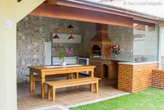 an outdoor kitchen with a table and bench in the middle of it, next to a brick oven