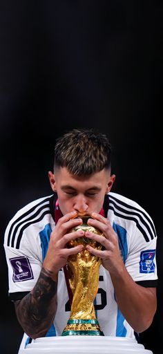 a man eating a sandwich while standing in front of a soccer trophy with his hands to his mouth