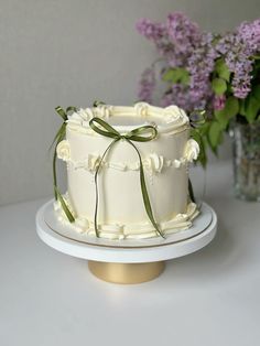 a white cake with green ribbon and flowers in the background