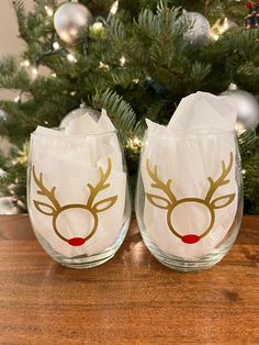 two wine glasses decorated with gold reindeer heads and red noses, sitting on a table next to a christmas tree