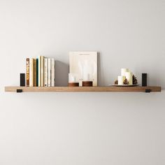 some books and candles are sitting on a wooden shelf above a bookcase in a white room