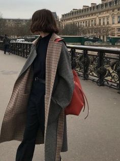 a woman is walking down the street wearing a coat and hat with a red handbag