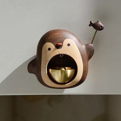 a monkey shaped object with a gold bowl in it's mouth hanging from the wall