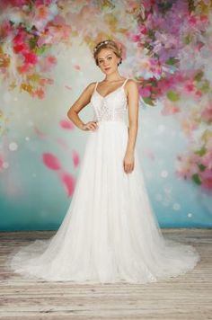 a woman standing in front of a floral backdrop wearing a white dress and headpiece