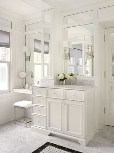 a white bathroom with two sinks, mirrors and a bench in front of the window