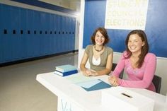 two women sitting at a desk in front of blue lockers with writing on them