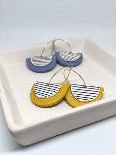 two yellow and blue earrings are on a white square plate with gold earwires