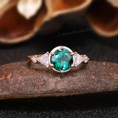 an emerald and diamond ring sitting on top of a rock