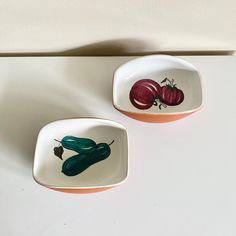 two bowls with vegetables painted on them sitting next to each other in front of a white wall