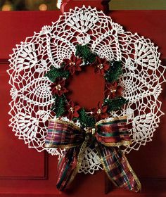 a white doily wreath on a red door with plaid ribbon and poinsettis