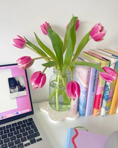 a laptop computer sitting on top of a desk next to a vase filled with pink tulips