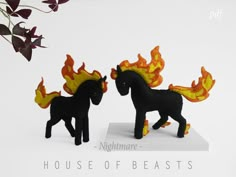 two small black horses with flames on their heads and tail, standing next to each other