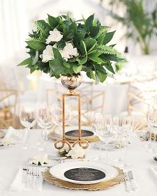 a table set with white and gold plates, silverware and flowers in a vase